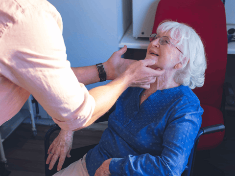 A caregiver performs a swallowing assessment on an older woman in a wheelchair, which is a common part of managing als and dysphagia.