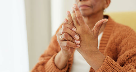 Elderly woman holding her hands in pain, illustrating the challenges arthritis sufferers face with daily tasks like brushing.