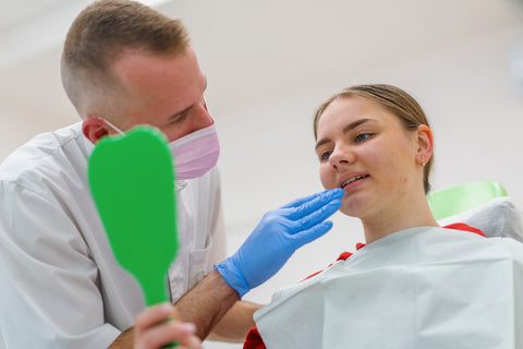 Young girl with sensory needs examining her teeth with a mirror during a dental visit