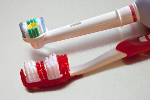 Side-by-side comparison of a manual toothbrush and an electric toothbrush on a clean white background.