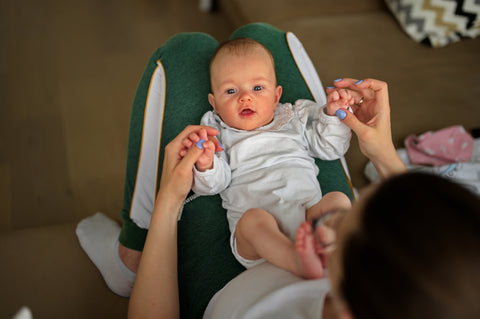 Small baby lying peacefully across a caregiver’s legs on a couch, symbolizing nurturing care and close attention to health needs.