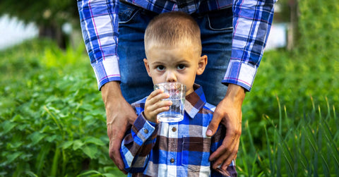 Young child being assisted while drinking water from a glass, illustrating support for swallowing difficulties.