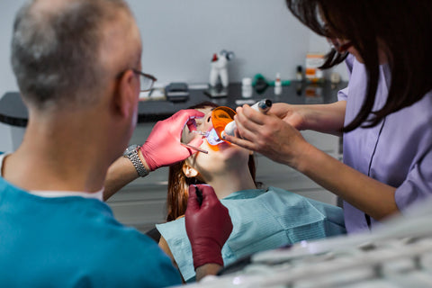 Two dentists working together to repair a patient’s teeth in a modern dental office, using tools and wearing protective gear.