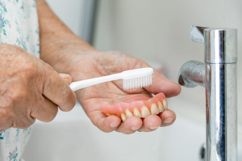 A close-up of someone gently brushing dentures with a soft-bristled toothbrush, focusing on thorough and careful cleaning.