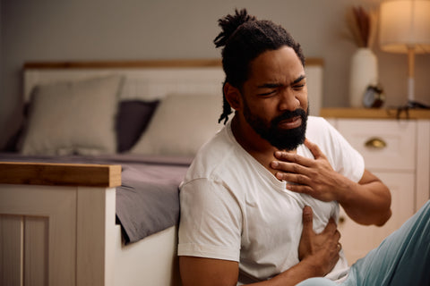 Person seated, clutching their chest and throat with a pained expression, illustrating heartburn and swallowing discomfort.